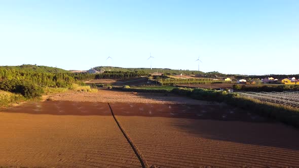 Aerial view of agriculture fields being watered and wind fans in the background, going backward