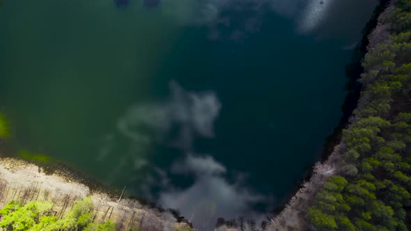 Blue lake with shape of heart with clouds reflected on water with trees around. Aerial at sunrise ti