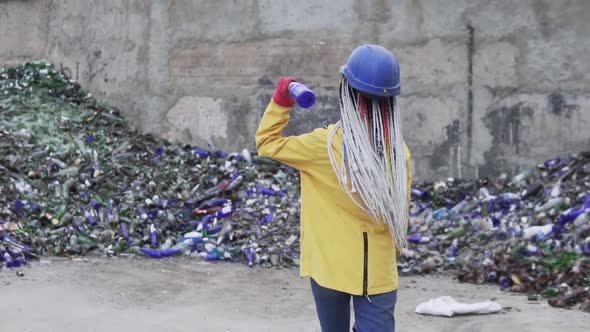 Woman in Hard Hat Standing Against the Pile of Broken Glass Used Bottles Next to the Wall