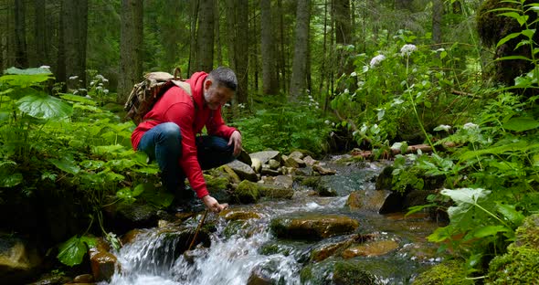 A Bearded Man with a Backpack Drinks Water From a Mountain Stream