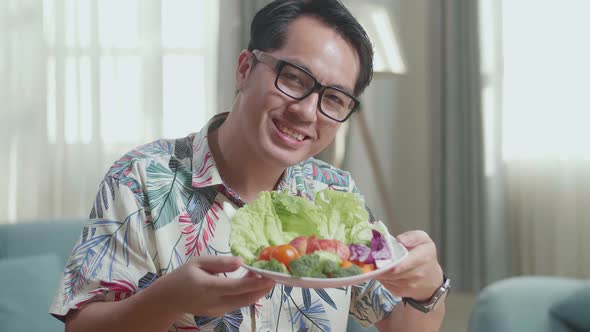 Close Up Of Smiling Asian Man Showing A Dish Of Healthy Food To Camera At Home