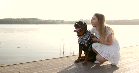 Young Woman Stroking Black Rottweiler on Lake Pier