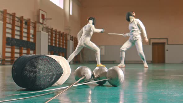 Two Young Women Fencers Having a Training in the School Gym - Gear on the Foreground