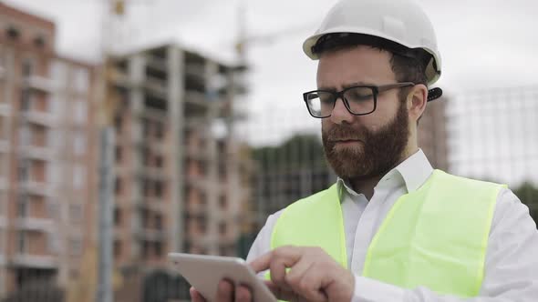 Architect Man Standing with Tablet on the Construction Site and Analyzing Scheme Project Plan