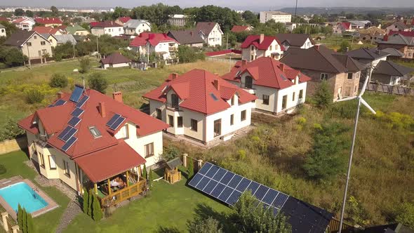 Aerial View of a Residential Private House with Solar Panels on Roof and Wind Generator Turbine
