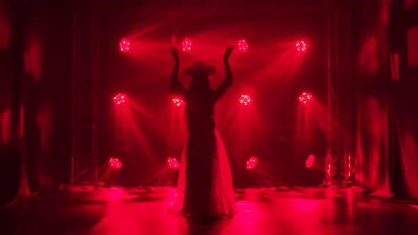 A Woman Dancer Is Silhouetted in Red Lights and Smoke Performing a Folk Dance. A Bright Brunette in