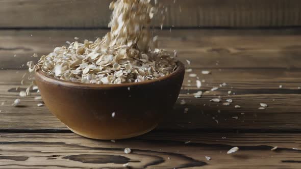Slow motion of oatmeal falling into a bowl on a wooden table.