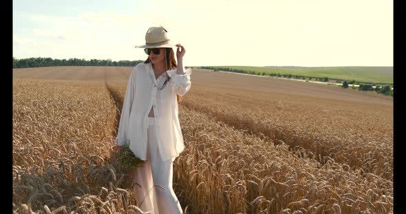 The Pregnant Girl with a Hat in the Field of Wheat on a Sunset
