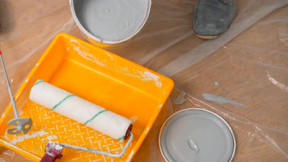 A Painter Pours Gray Paint From a Bucket Into a Tray for Further Painting the Walls