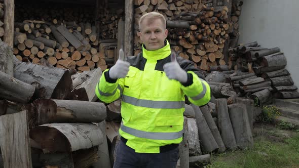 Lumberjack in Reflective Jacket. Man Woodcutter Show Thumbs Up. Sawn Logs, Firewood Background