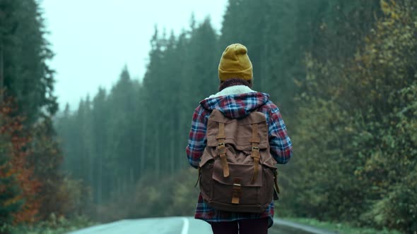 Back View Woman Hitchhiker Traveler with Backpack Walks Alog Road Outdoors in Cold Wet Foggy Autumn