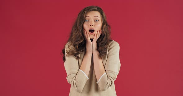 Studio Portrait Caucasian Woman Stands on Red Background in Delight Opens Her Mouth in Surprise