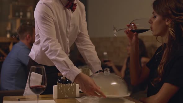 Beautiful Caucasian Young Female Drinking Wine From Glass at Restaurant While Male Waiter Bringing