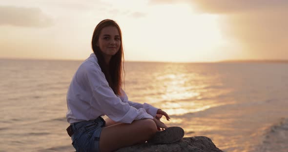 Young Woman Showing Let It Rock Gesture Sitting Near Sea