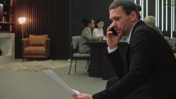 Man in Suit Talk on the Phone While Employees Sit at Meeting in Modern Office