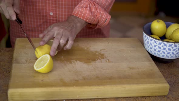 As camera slides from left to right, a chef cuts fresh lemons on a thick wood cutting board.  A juic