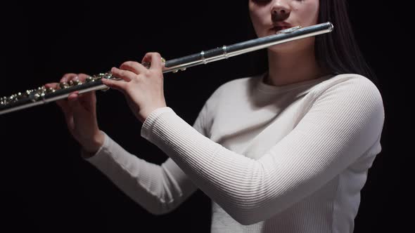 Female Musician Brings Flute to Lips and Plays Classical Music Dark Background in Studio Front View