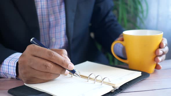 Man Hand Writing on Notepad While Sited