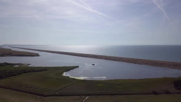 Wide aerial tracking forward to the fleet lagoon at the west end of the shingle beach. Sun reflectio