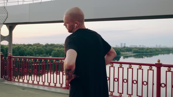 Man Runner in Black Sports Uniform Doing Warmup Before Jogging on the Pedestrian Bridge at Sunrise