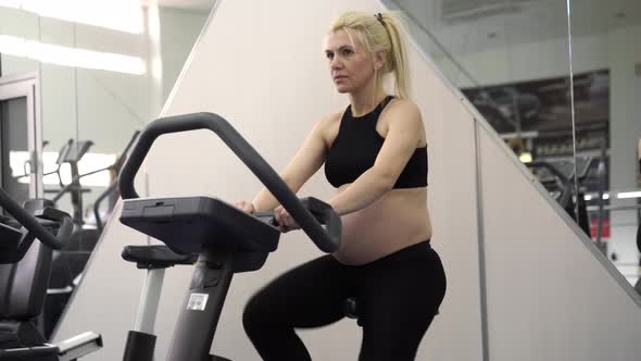 Pregnant Woman Training Exercise Bike in Gym Cardio Exercises on Running Simulator