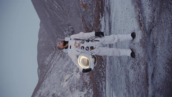 Astronaut Stands with a Helmet in His Hand By the Hills