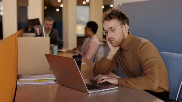 Tired Caucasian Young Man Sitting at Table and Feeling Bored While Working Hardly