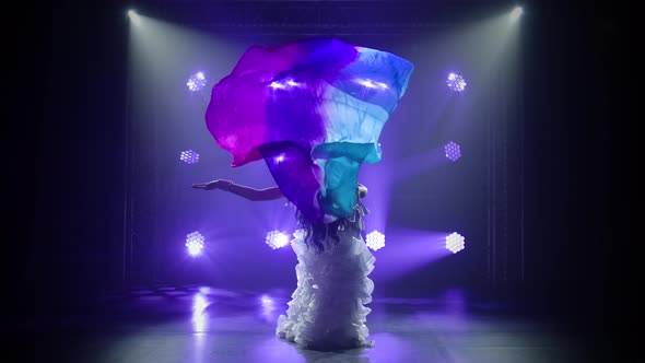 Female Belly Dancer in a White Oriental Costume Dancing with Silk Cloth. Shot in a Dark Studio with