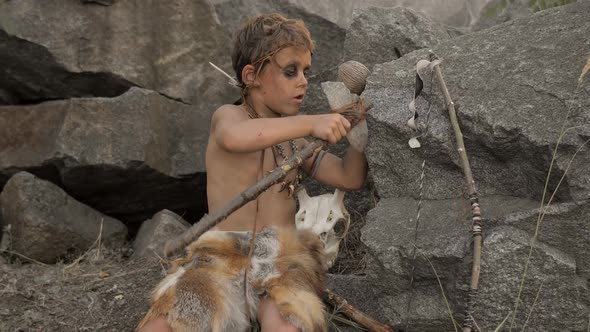 Caveman Manly Boy Making Primitive Stone Weapon in Camp