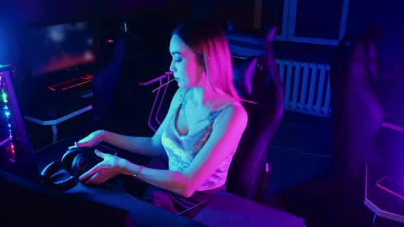 Gaming Concept - Young Attractive Gamer Woman Sits in the Chair in Neon Gaming Club and Sucking a