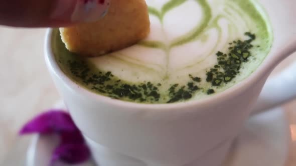 Dipping Cookie into Hot Creamy Matcha Powder Froth Latte Art