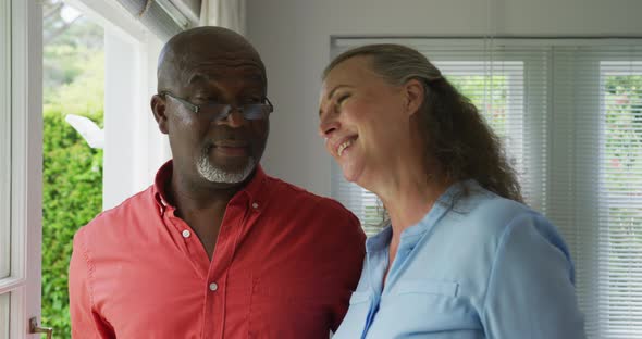 Happy senior diverse couple wearing shirts and embracing in living room