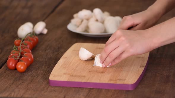 Woman is cutting mushroom on kitchen table.