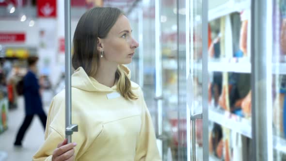 Woman Buys Frozen Food in a Supermarket. An Attractive Young Woman Stands Near the Freezer 