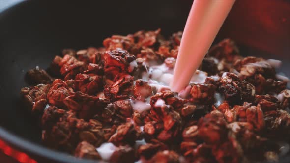 Close-up of pouring milk into a black bowl with granola. Oatmeal with nuts and seeds.