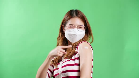 Young Asian woman pointing to her arm after being vaccinated against covid-19 in studio with chroma