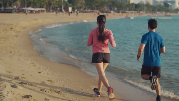 Asian runners fitness couple running training on the beach.