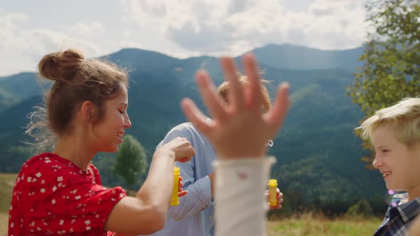 Family Playing Blowing Soap Bubbles in Summer Mountains