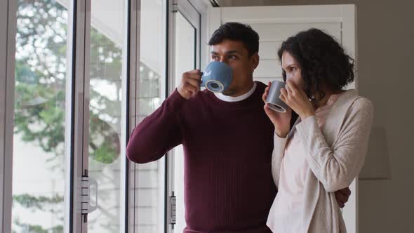 Romantic hispanic couple embracing standing in window having coffee