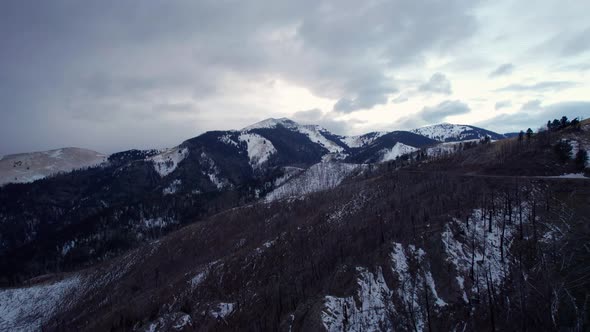 Panning drone shot of large snowy mountain peaks with a winding road