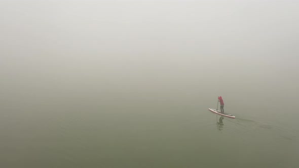 Alone Man is Floating on a Board on a River in a Very Thick Fog
