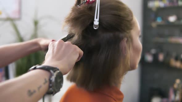 Hairdresser Straightens Hair of Sitting Woman with a Hair Iron in Beauty Studio