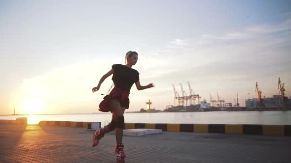 Young Stylish Funky Girl with Green Hair Riding Roller Skates and Dancing Near Sea Port During