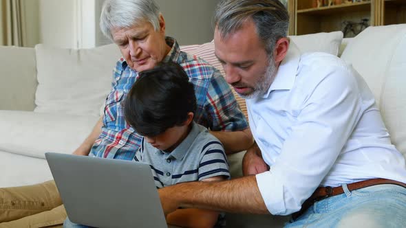 Son, father and grandfather sitting on sofa using laptop in living room