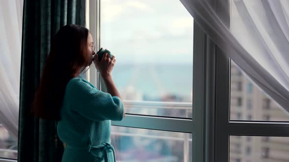 Relax Time at Home at Weekend Woman is Looking at Window Enjoying City View and Drinking Hot Tea