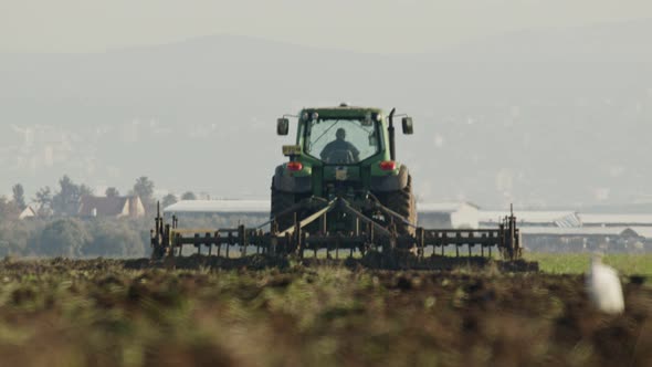 Tractor cultivating a green field in slow motion.