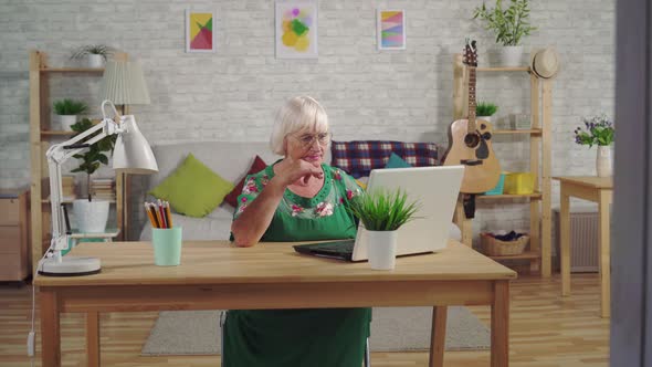 Grandma Is Typing on Her Laptop While Sitting at the Living Room Table