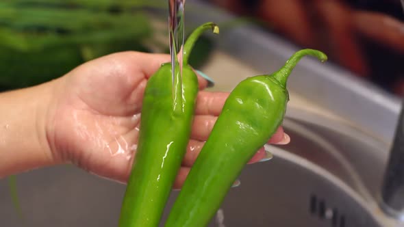 Closeup of Young Girl Washing Chili Peppers in the Sink at Home in the Kitchen