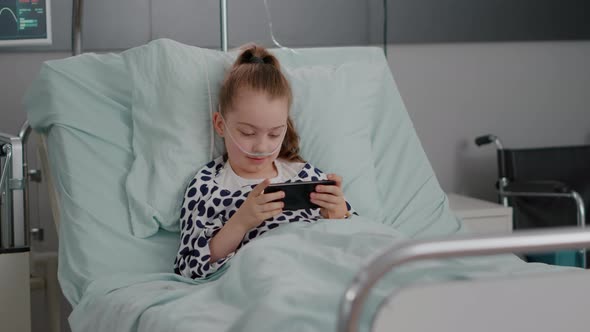 Sick Little Child Resting in Bed Playing Online Video Games Using Smartphone