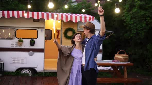 Young Couple Embracing Standing in Front Trailer They Living in with Sparklers Celebrating Dancing